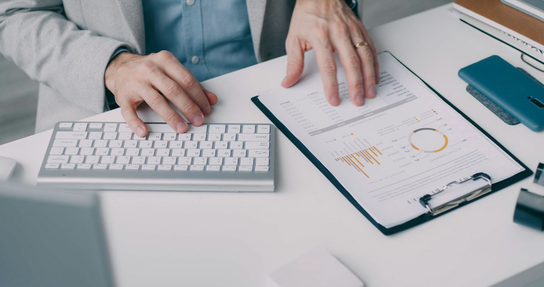 Handen die een financieel rapport met grafieken doornemen naast een toetsenbord